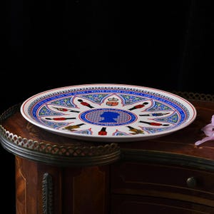 Puede incluir: Un plato conmemorativo de cer&aacute;mica blanca con una silueta azul de la Reina en el centro, rodeado de ilustraciones de guardias reales y motivos florales. El texto del borde dice Silver Jubilee 1952-1977 y God Save The Queen.
