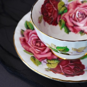 Peut inclure: Un ensemble tasse et soucoupe en porcelaine blanche orn&eacute; d'un motif floral compos&eacute; de roses rouge fonc&eacute; et roses avec des feuilles vertes. Les bords de la tasse et de la soucoupe sont finis par un fin liser&eacute; dor&eacute; r&eacute;fl&eacute;chissant et m&eacute;tallique.