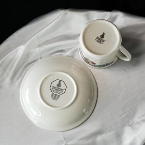 Może przedstawiać: Biały zestaw filiżanki i spodka z kwiatowym wzorem. Filiżanka jest do g&oacute;ry dnem, odsłaniając stempel Royal Doulton Autumn's Glory. Spodek r&oacute;wnież wyświetla stempel Royal Doulton. Zestaw znajduje się na białej, teksturowanej powierzchni.