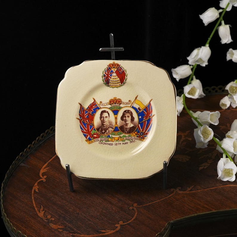 Puede incluir: Un plato de cer&aacute;mica cuadrado de color crema que conmemora al Rey Jorge VI y a la Reina Isabel. El centro muestra retratos, banderas, una corona y el texto "H.M. KING GEORGE VI H.M. QUEEN ELIZABETH CROWNED 12TH MAY 1937."