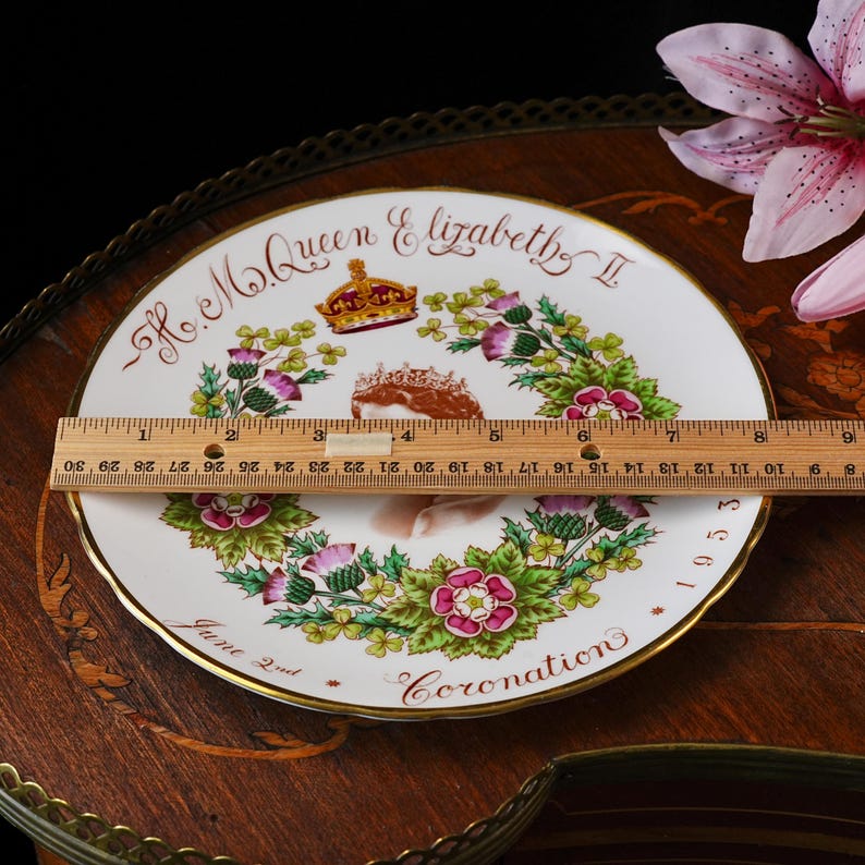 Op de afbeelding: Een wit herdenkingsbord van porselein met een portret van koningin Elizabeth II, een kroon en bloemmotieven. De tekst luidt H.M. Queen Elizabeth II, June 2nd, 1953 en Coronation. Een houten liniaal toont een diameter van 20,3 cm.