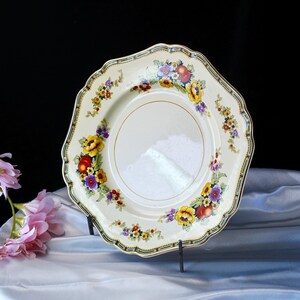 Puede incluir: Plato vintage de color crema con borde festoneado, adornado con un vibrante estampado floral en amarillo, rojo y morado. El plato tiene un borde dorado y un borde decorativo. Una pieza cl&aacute;sica para servir o exhibir.