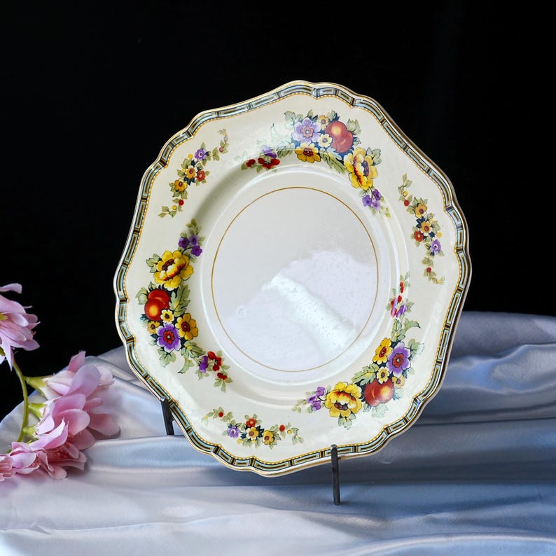 Puede incluir: Plato vintage de color crema con borde festoneado, adornado con un vibrante estampado floral en amarillo, rojo y morado. El plato tiene un borde dorado y un borde decorativo. Una pieza cl&aacute;sica para servir o exhibir.