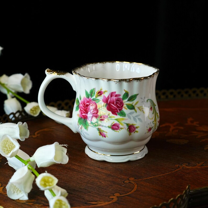 Peut inclure: Une tasse &agrave; th&eacute; en porcelaine blanche avec un bord festonn&eacute; dor&eacute;, une anse incurv&eacute;e aux accents dor&eacute;s et un motif floral de roses roses avec des feuilles vertes. La tasse pr&eacute;sente un corps cannel&eacute; et une base sur pied avec un bord dor&eacute;.