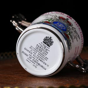 May include: A white Paragon fine bone china mug commemorating the Silver Wedding of Queen Elizabeth II and Prince Philip, Duke of Edinburgh. The mug has a silver handle and rim, with a royal crest and text.