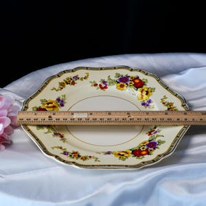 Puede incluir: Plato octogonal color crema con un dise&ntilde;o floral con flores rojas, amarillas y moradas. El plato tiene un borde dorado y un borde decorativo. El plato mide aproximadamente 25 cm de di&aacute;metro.
