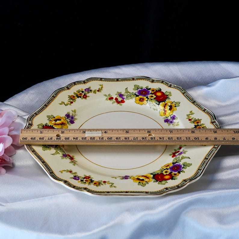 Puede incluir: Plato octogonal color crema con un dise&ntilde;o floral con flores rojas, amarillas y moradas. El plato tiene un borde dorado y un borde decorativo. El plato mide aproximadamente 25 cm de di&aacute;metro.