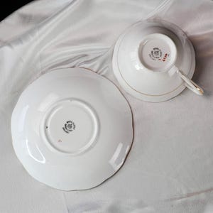 Op de afbeelding: Witte theekop en schotel set met gouden rand. De theekop staat ondersteboven en toont de Royal Albert stempel. De schotel heeft een geschulpte rand. De set staat op een wit, getextureerd oppervlak.