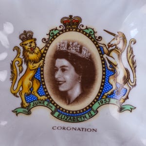 May include: A white ceramic commemorative dish featuring a central portrait of Queen Elizabeth II wearing a crown. The portrait is framed by a lion and a unicorn, with a crown above and text reading June 2nd, 1953, Elizabeth II, and Coronation.