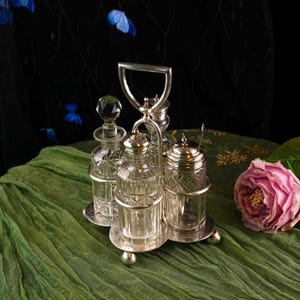 Könnte beinhalten: Ein Vintage-Gewürzset aus versilbertem Metall mit vier durchsichtigen Glasflaschen und -gläsern. Das Set enthält einen Griff, eine Zuckerdose mit Löffel und zwei Flaschen mit Kristallstopfen. Das Set steht auf einem grünen Tuch mit einer rosa Rose.