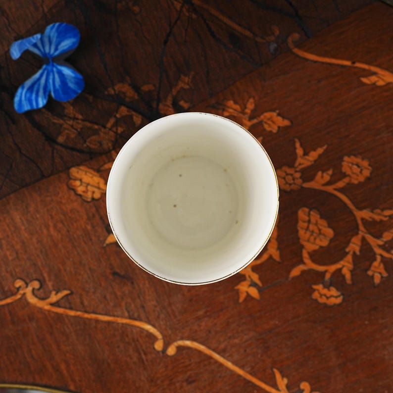 Puede incluir: Una taza de cer&aacute;mica blanca con un borde dorado vista directamente desde arriba. El interior de la taza es liso y de color blanco roto con peque&ntilde;as manchas oscuras visibles en la base. La taza tiene forma cil&iacute;ndrica y un borde dorado fino.