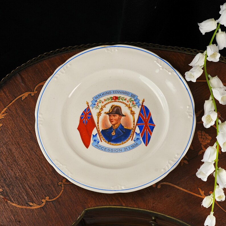 K&ouml;nnte beinhalten: Ein cremefarbener Gedenkteller aus Keramik mit einem zentralen Portr&auml;t von H.M. King Edward VIII in Milit&auml;runiform, flankiert von zwei Flaggen, mit dem Text H.M. KING EDWARD VIII und ACCESSION 21.1.1936, verziert mit einem d&uuml;nnen blauen Rand.