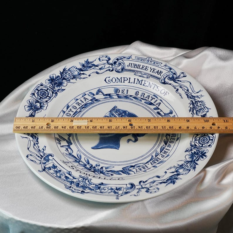 May include: White and blue commemorative plate with a portrait of a woman, possibly Queen Victoria, and the text "Jubilee Year Compliments of Dei Gratia". The plate is approximately 12 inches in diameter.