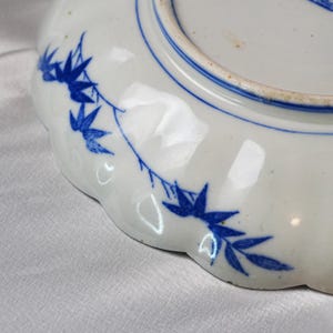 Puede incluir: Plato de cer&aacute;mica blanca con borde festoneado y dise&ntilde;o floral azul. El plato presenta un borde pintado de azul y un delicado patr&oacute;n de hojas y ramas azules. El plato es probablemente vintage o antiguo.