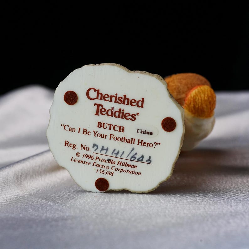 Op de afbeelding: Een "Cherished Teddies" beeldje met de tekst "Can I Be Your Football Hero?" en de naam "BUTCH". De basis is gebroken wit met bruine accenten en tekst. Het beeldje is gemaakt in China.