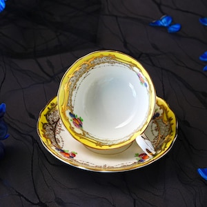 Peut inclure: Un ensemble tasse et soucoupe en porcelaine avec un bord jaune vif et des d&eacute;tails en filigrane dor&eacute;. L'int&eacute;rieur et la base blancs sont orn&eacute;s de petits motifs floraux color&eacute;s en rouge, bleu et vert, compl&eacute;t&eacute;s par un d&eacute;licat motif en treillis.