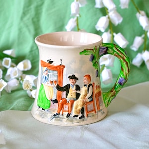 May include: Cream-colored ceramic mug with a detailed scene of people in a pub. The handle is green and brown, resembling a tree branch. The mug features a painted scene of a bartender and patrons. A charming collectible.