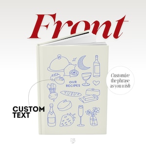May include: A cream-colored hardcover recipe book featuring blue line art illustrations of food and drink items, including a cloche, lemon, crescent moon, wine bottle, bread, cheese, strawberry, and flowers, with the text OUR RECIPES printed in the center.