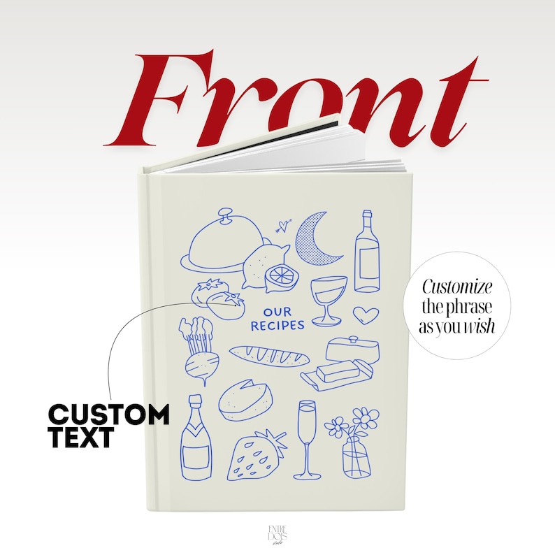May include: A cream-colored hardcover recipe book featuring blue line art illustrations of food and drink items, including a cloche, lemon, crescent moon, wine bottle, bread, cheese, strawberry, and flowers, with the text OUR RECIPES printed in the center.