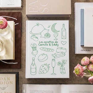 May include: A white hardcover book titled Les recettes de Camille & Eddy in green text, featuring green line art illustrations of food and drink items including a cloche, lemon, crescent moon, wine bottle, baguette, cheese, and a strawberry.