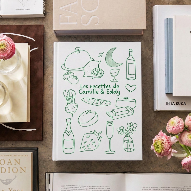 May include: A white hardcover book titled Les recettes de Camille & Eddy in green text, featuring green line art illustrations of food and drink items including a cloche, lemon, crescent moon, wine bottle, baguette, cheese, and a strawberry.