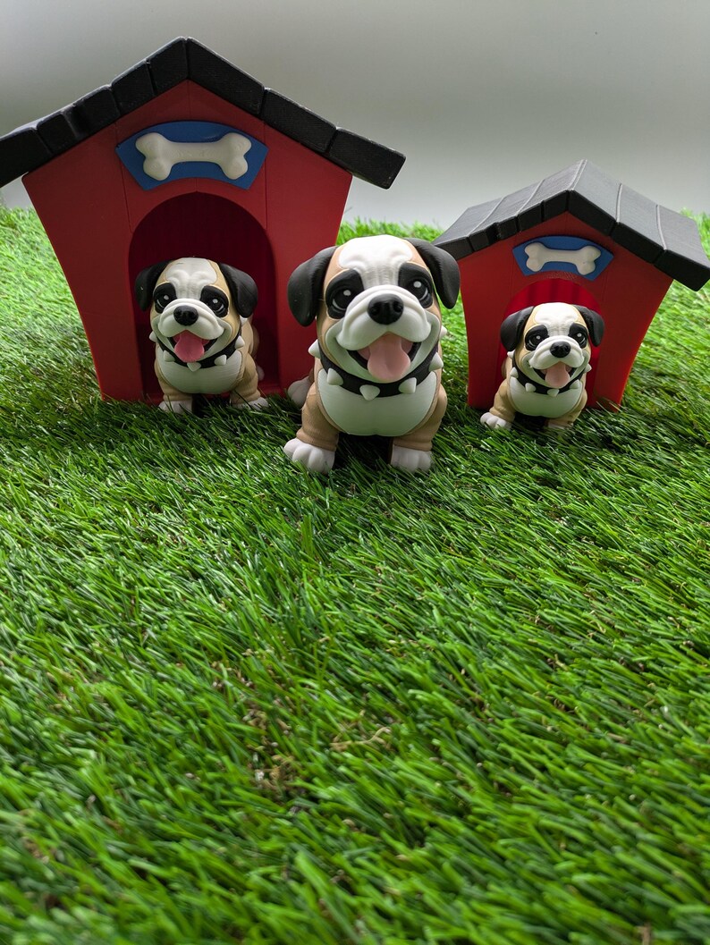 Op de afbeelding: Drie bruine en witte bulldog-figuurtjes, elk staand voor een rood en zwart hondenhok met een wit bot op het dak. De hondenhokken zijn van verschillende grootte, en de figuurtjes kijken allemaal naar voren met hun tongen uitgestoken.