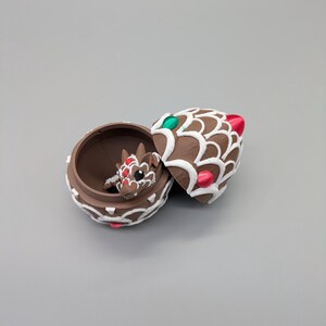 May include: A brown, decorative trinket box with a dragon figurine inside. The box is open, revealing the dragon and the interior. The box and lid are decorated with white icing-like designs and red and green accents.