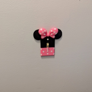 May include: A black light switch cover with pink polka dots and a pink bow. The switch cover is shaped like Mickey Mouse's head.