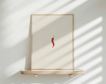 May include: A framed print of a single red chili pepper on a white background. The print is displayed on a light wood shelf.