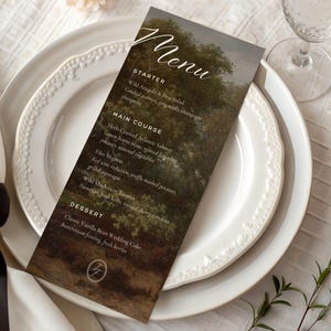 May include: A printed menu card with a landscape painting design, featuring the word "Menu" in elegant script. The menu is placed on a white plate with a decorative rim, alongside a folded napkin and a wine glass. The menu lists starters, main courses, and desserts.