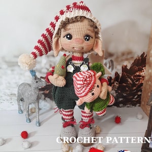 Könnte beinhalten: Eine gehäkelte Weihnachts-Elfenpuppe, die eine kleine gehäkelte Elfenpuppe hält. Die größere Elfe trägt eine rot-weiß gestreifte Mütze, ein grün-weiß gestreiftes Hemd und eine grüne Hose. Die kleinere Elfe trägt eine rot-weiß gestreifte Mütze und ein grünes Hemd. Der Text "CROCHET PATTERN" ist am unteren Rand des Bildes sichtbar. Die Flaggen der Türkei und der Vereinigten Staaten sind ebenfalls sichtbar.