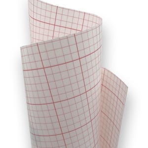 Op de afbeelding: Een rol transparant transferpapier met een rasterpatroon. Het papier is wit met een rood raster. Het papier is opgerold en toont het rasterpatroon. Geschikt voor knutsel- en designprojecten, gemeten in centimeters.