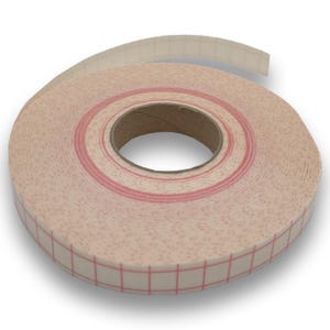 Könnte beinhalten: Eine Rolle beiges Klebeband mit einem roten Gittermuster und einem rosa Streifen. Das Band ist aufgerollt und zeigt einen Pappkern. Das Band ist für Bastelarbeiten oder andere Projekte bestimmt.