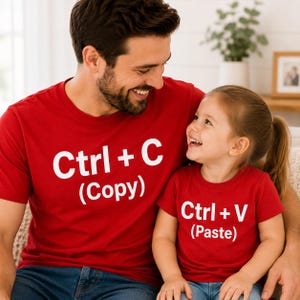 May include: A red short-sleeved t-shirt with white text that reads Ctrl + C (Copy) and a matching red short-sleeved t-shirt with white text that reads Ctrl + V (Paste), both featuring a crew neckline and a standard cotton-style fabric construction.