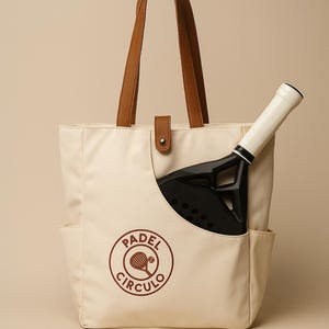 May include: Cream-colored tote bag with brown leather handles and a padel racket. The bag has a side pocket and a circular logo that says "Padel Circulo" in brown.