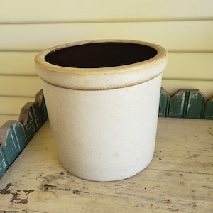 May include: A white ceramic crock with a brown rim sits on a green and white painted wooden surface.