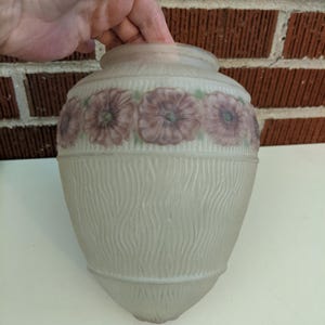 Może przedstawiać: Biały, matowy klosz lampy wykonany ze szkła z fakturowanym, falistym wzorem i paskiem różowych kwiatów wokół górnej części.