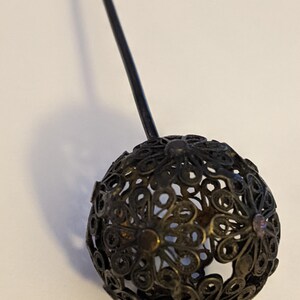 May include: A black filigree ball with a long black stem. The ball is made of intricate metalwork and has small, clear rhinestones.