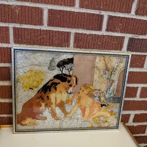 May include: A framed vintage illustration of a girl and a dog looking at each other. The girl is wearing a pink dress and the dog is brown and black. The background is a light brown with a tree and flowers.