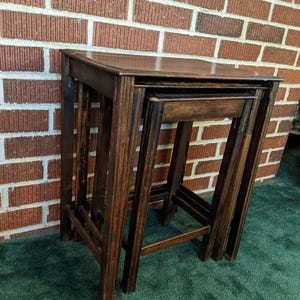 May include: A set of three nesting tables crafted from dark brown wood. The tables feature a rectangular top surface and four straight legs each, designed to slide neatly underneath one another for compact storage when not in use.