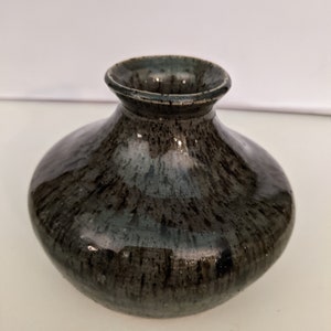 May include: A small, dark gray ceramic vase with a speckled glaze. The vase has a rounded body and a slightly flared opening.