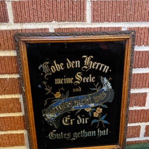 May include: A framed antique mirror with a black background and gold lettering. The mirror features a German inscription that reads "Lobe den Herrn, meine Seele und vergiß nicht was Er dir Gutes gethan hat."