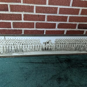 May include: A framed black and white photograph of a large group of people in uniform. The photograph is rectangular and has a dark frame. The background is a brick wall and green carpet.