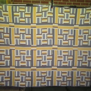 Puede incluir: Una colcha con un patrón geométrico en tonos de amarillo, azul, marrón y blanco.