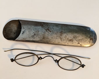 Occhiali da vista antichi con montatura in filo metallico e custodia in metallo con design di gru incisa
