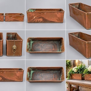 May include: A rectangular copper planter featuring a weathered patina finish and brass lion head handles with attached rings on each side. The container has a deep interior with visible oxidation and a sturdy, elongated metal construction.
