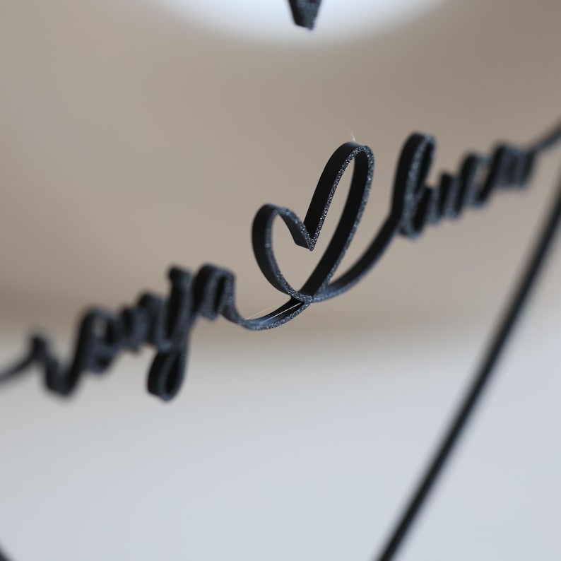 May include: Black cursive text with the words "Sonya I love you" and a heart symbol. The text is in a script font and appears to be made of a textured material. The background is a soft, neutral color.