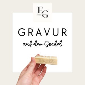 Könnte beinhalten: Ein helles Holzstück mit dem eingravierten Datum "31.07.2025". Der Block wird in einer Hand gehalten. Der Text "GRAVUR auf den Sockel" wird in schwarzer Schrift angezeigt.