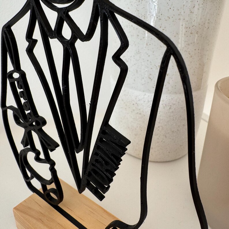 May include: Black metal silhouette of a person wearing a suit and tie. The silhouette is standing on a wooden base. The word "MORGAN" is written on the suit jacket.