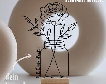 May include: A black metal rose and leaves design in a mason jar, mounted on a wooden base. The words "EWIGE ROSE" are at the top, and "Ich liebe dich" is written on the jar. The words "dein Spruch" are also present.